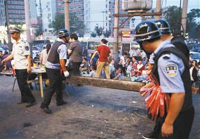 6月13日晚8點(diǎn)，朝陽路和青年路交叉口西側(cè)，一次聯(lián)合執(zhí)法行動中，輔警與協(xié)管抬走商戶的燒烤用具。新京報記者 尹亞飛 攝