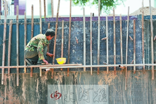 　　烈日下，狹窄的架子上，工人正用錘子固定樁基。