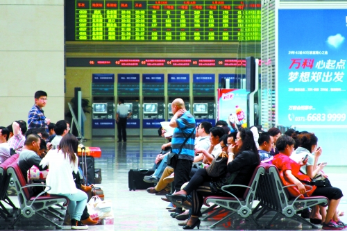 候車(chē)大廳溫度很高，一名乘客一手扇風(fēng)、一手擦汗