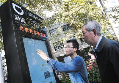 10月15日，滴滴工作人員（左）指導(dǎo)乘客使用“滴滴車站”的電子屏預(yù)約出租車。