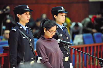 被告人盧梅低著頭，站在朝陽法院刑事審判庭的被告席上。