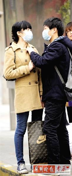 公交站臺上，一對年輕人戴著口罩，系緊衣領。